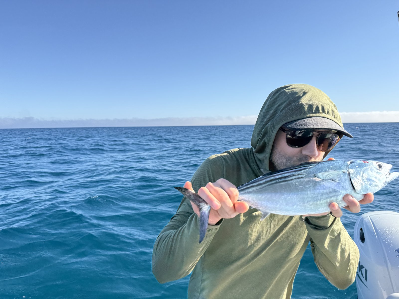 A man in a green hoodie kissing the bonito he just caught.