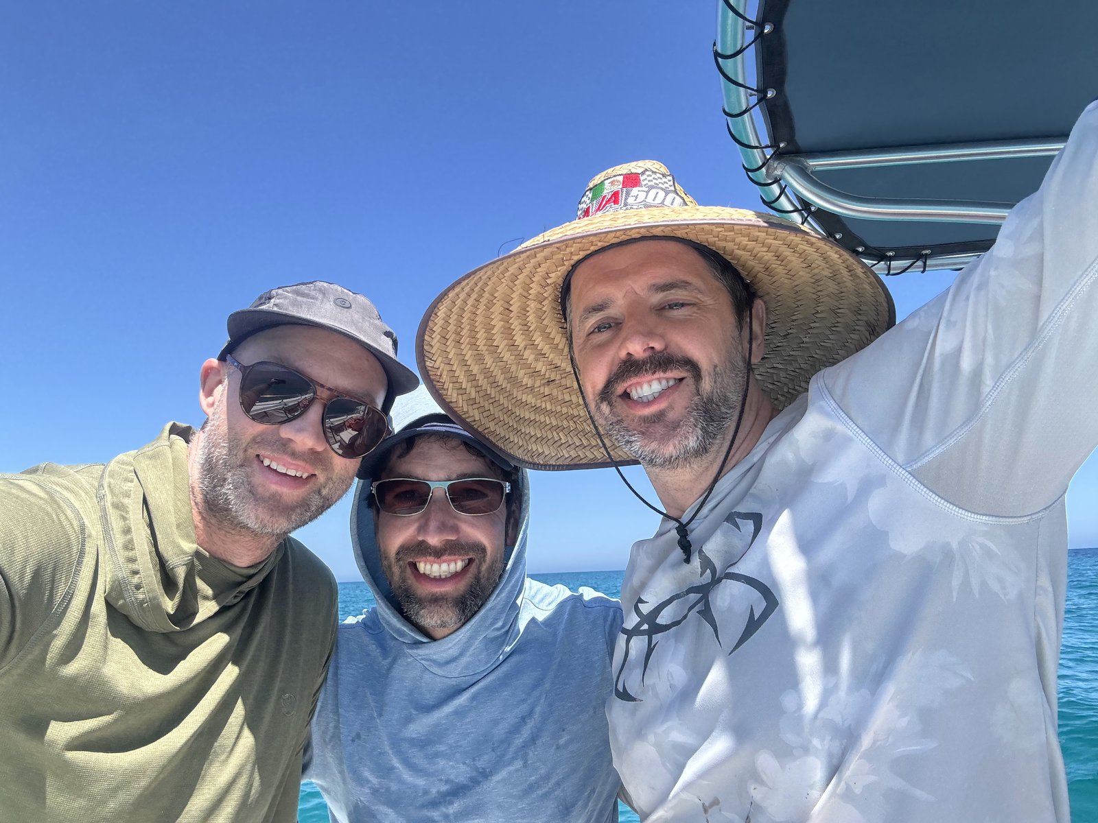 Three men taking a smiling selfie on the boat under the bright sun.